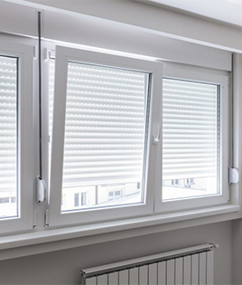 Volets roulants manuels partiellement fermés sur trois fenêtres blanches. L’une des fenêtres est ouverte en oscillo-battant, tandis que les deux autres sont fermées.