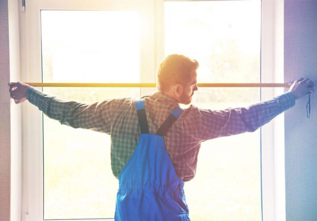 Artisan menuisier AMCC mesurant une fenêtre blanche au domicile d’un client.