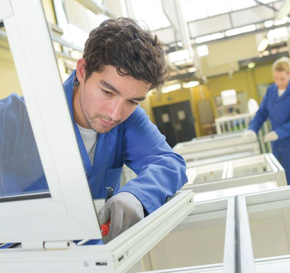 Assemblage d’une fenêtre blanche par un ouvrier menuisier dans l’usine de fabrication AMCC.