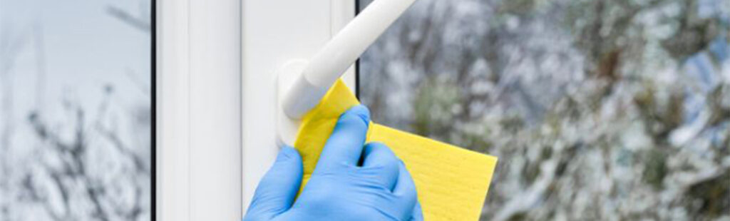 Entretien de fenêtre : Main nettoyant en douceur le cadre extérieur d’une fenêtre avec une éponge humide, la poignée étant visible au premier plan.