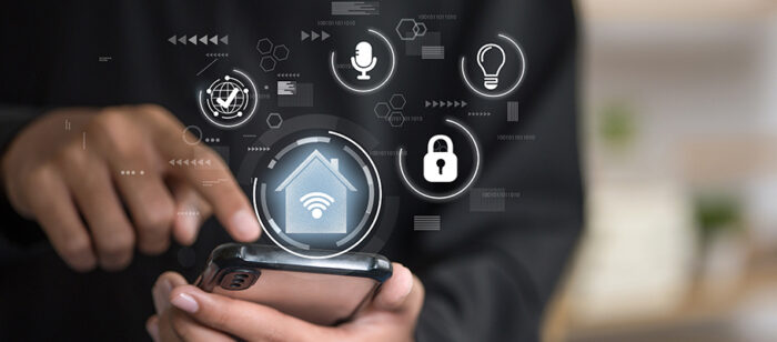Image montrant un zoom d'une main sur un téléphone portable avec une série d'icônes permettant de piloter une maison intelligente à distance grâce à la domotique
