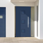 Photo d'ambiance d'une porte d'entrée aluminium zoé couleur bleue, vue de l'extérieur d'une maison moderne avec porte de garage bleue assortie.