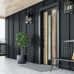 Photo d'ambiance d'une porte prestige gamme Nature modèle Daphné avec décor chêne blanchi sur une façade de maison à la fois contemporaine et charmante avec un lambris tout en noir et des lanternes extérieures au style classique et chic