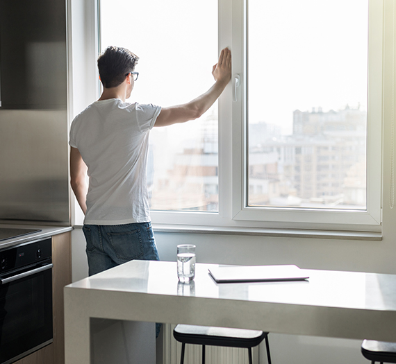 Homme devant une fenêtre PVC admirant la vue depuis son immeuble