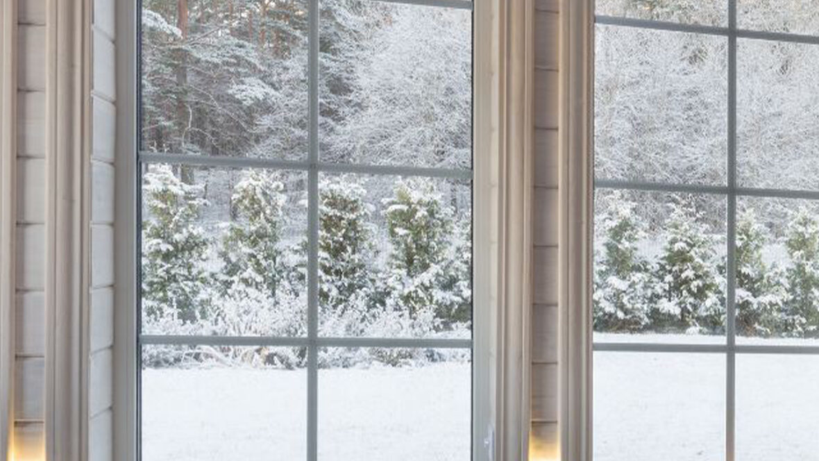 Zoom sur deux baies vitrées en PVC dans une chambre à coucher. À travers les vitres, on distingue un paysage hivernal couvert de neige. À l’intérieur, plusieurs bougies allumées diffusent une lumière douce et orangée, créant une atmosphère calme, intime et cosy malgré le froid extérieur.