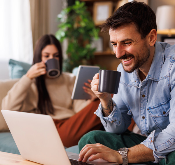 Photo d'un couple installé dans le salon chez eux en train de configurer leur porte d'entrée sur le configurateur AMCC sur un ordinateur relax et buvant un café
