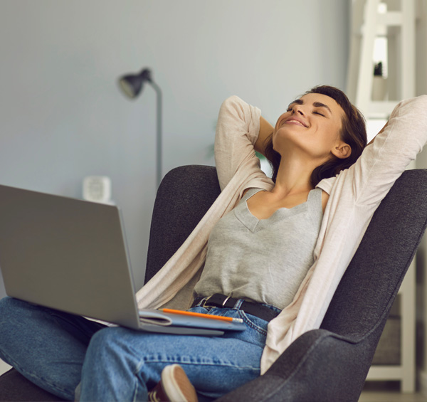 Photo d'une femme souriante relaxée dans son fauteuil en train de s'étirer avec un ordinateur sur les genoux rêvant à son projet fenêtres et portes avec AMCC