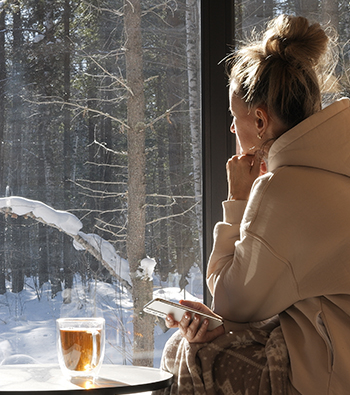 Femme devant sa fenêtre au soleil, isolée de la neige à l'extérieur
