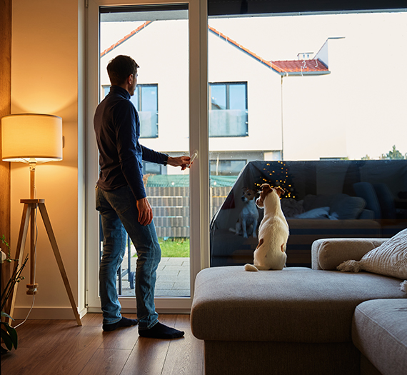 Homme devant la baie vitrée de sa maison avec son chien