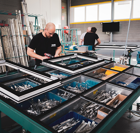 Opérateur de production qui assemble une fenêtre en aluminium dans l'usine SNM de La Bresse