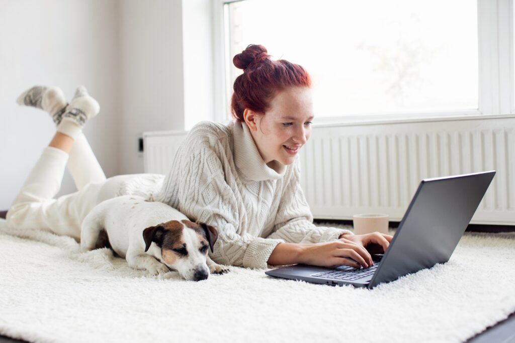 Une jeune femme, avec son chien allongé à côté d’elle, recherche sa future porte d’entrée AMCC sur son ordinateur.